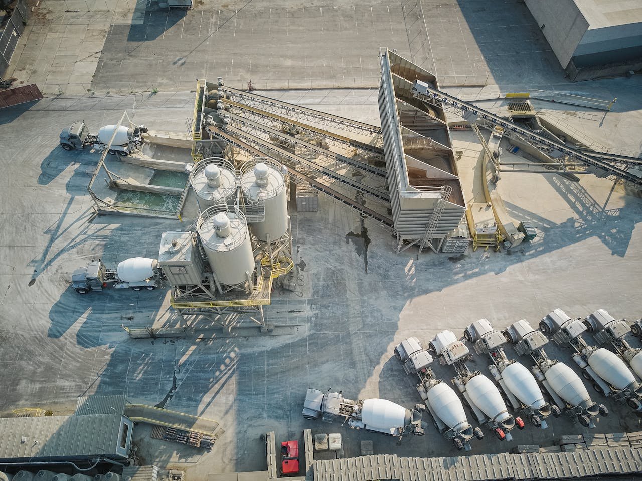 A drone-captured aerial view of an industrial concrete mixing plant with trucks and machinery.